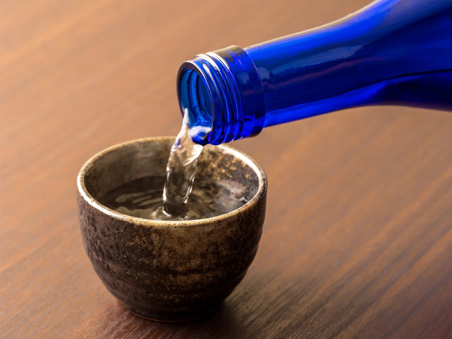 青い一升瓶からぐい呑みに日本酒を注いでいる